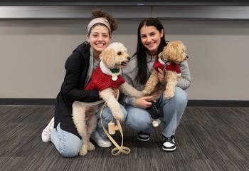 Two female students kneel down with their dogs