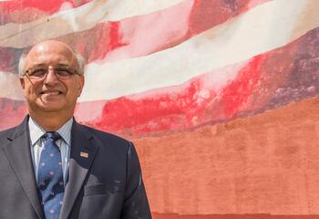 Ralph Galati '70 standing in front of an American flag mural