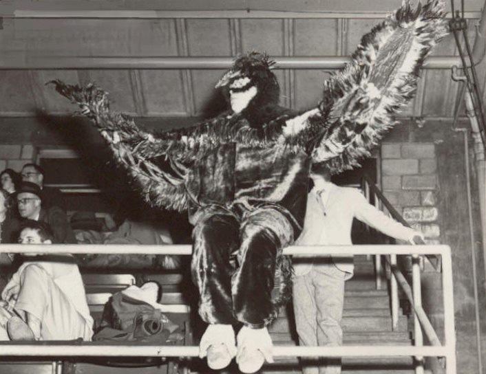 Black and white photo of Jim Brennan in the Hawk mascot sitting on a bleacher railing
