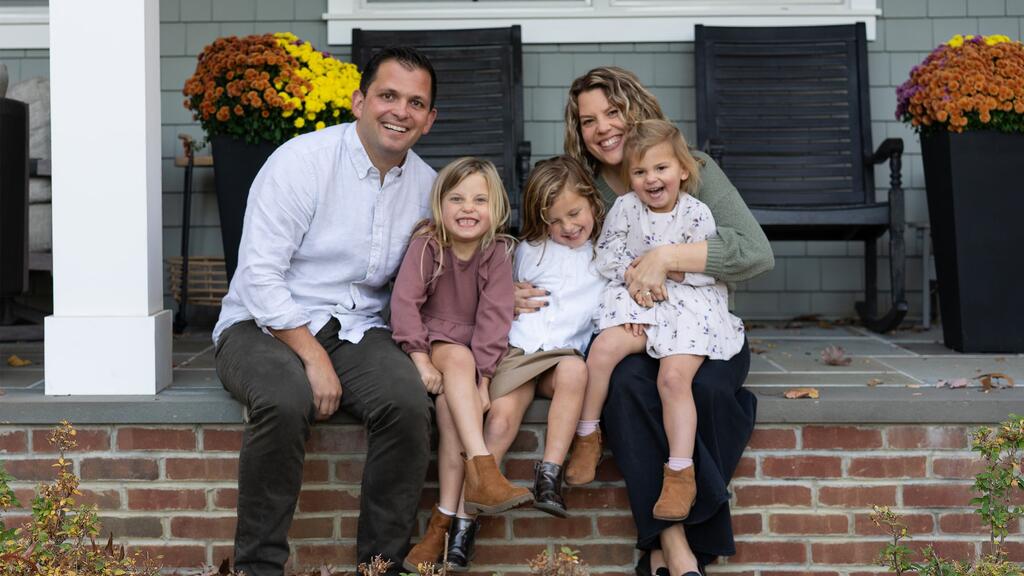 Ryan and Holly Moscatiello seated on their porch with their three daughters