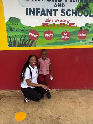 Kimisha Simpson, MS '16, EdD '25, kneels next to a child in a red uniform.