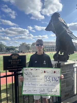 Jack Pavlovcak ’29 holding a large check for $55,136 in front of Sweeney Field.