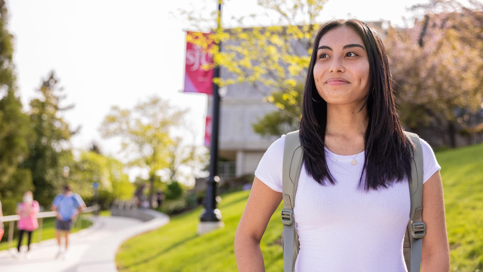 Female student standing on campus looking into the distance smiling