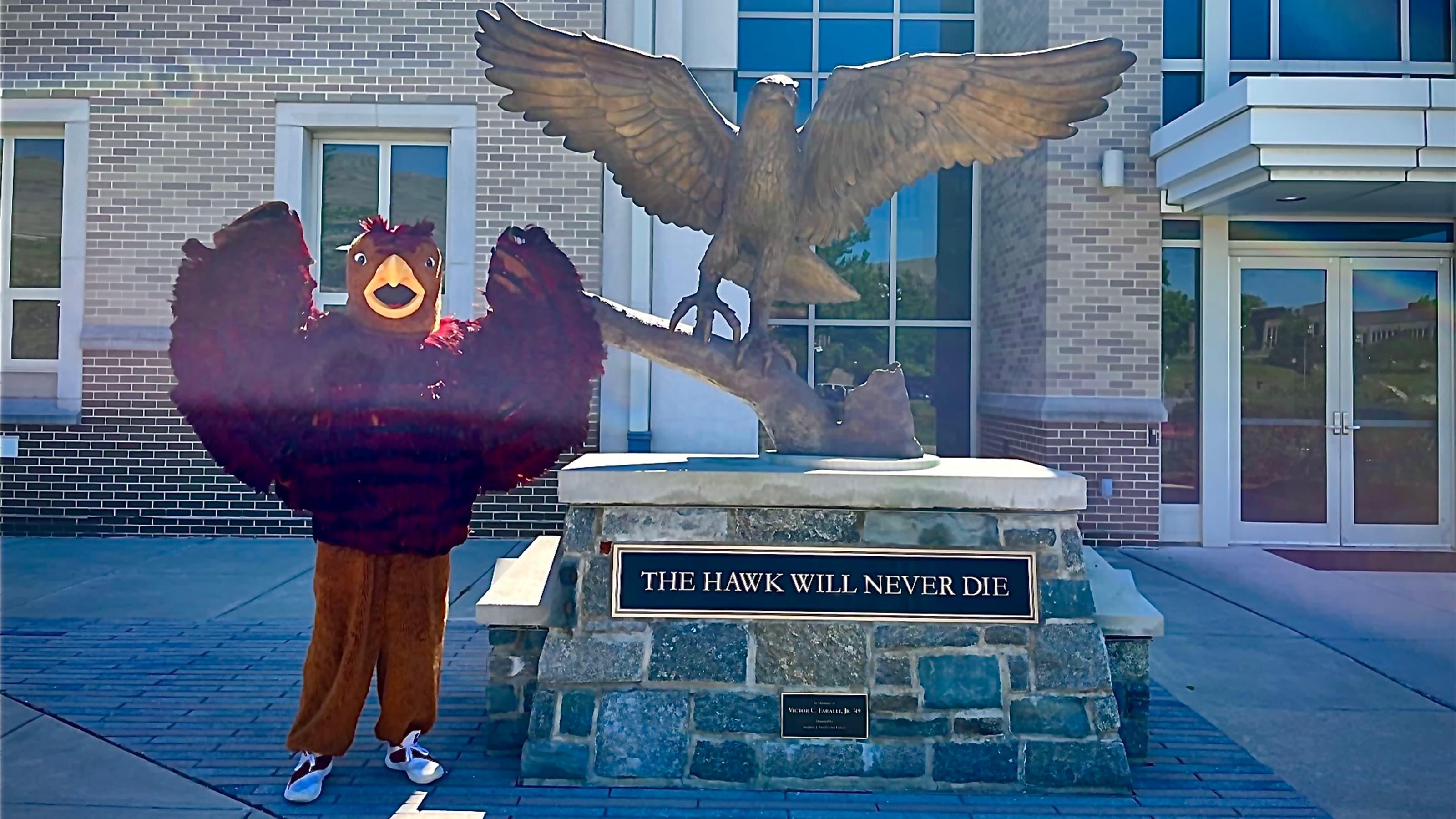 Hawk mascot in front of Hawk statue at Hagan Arena