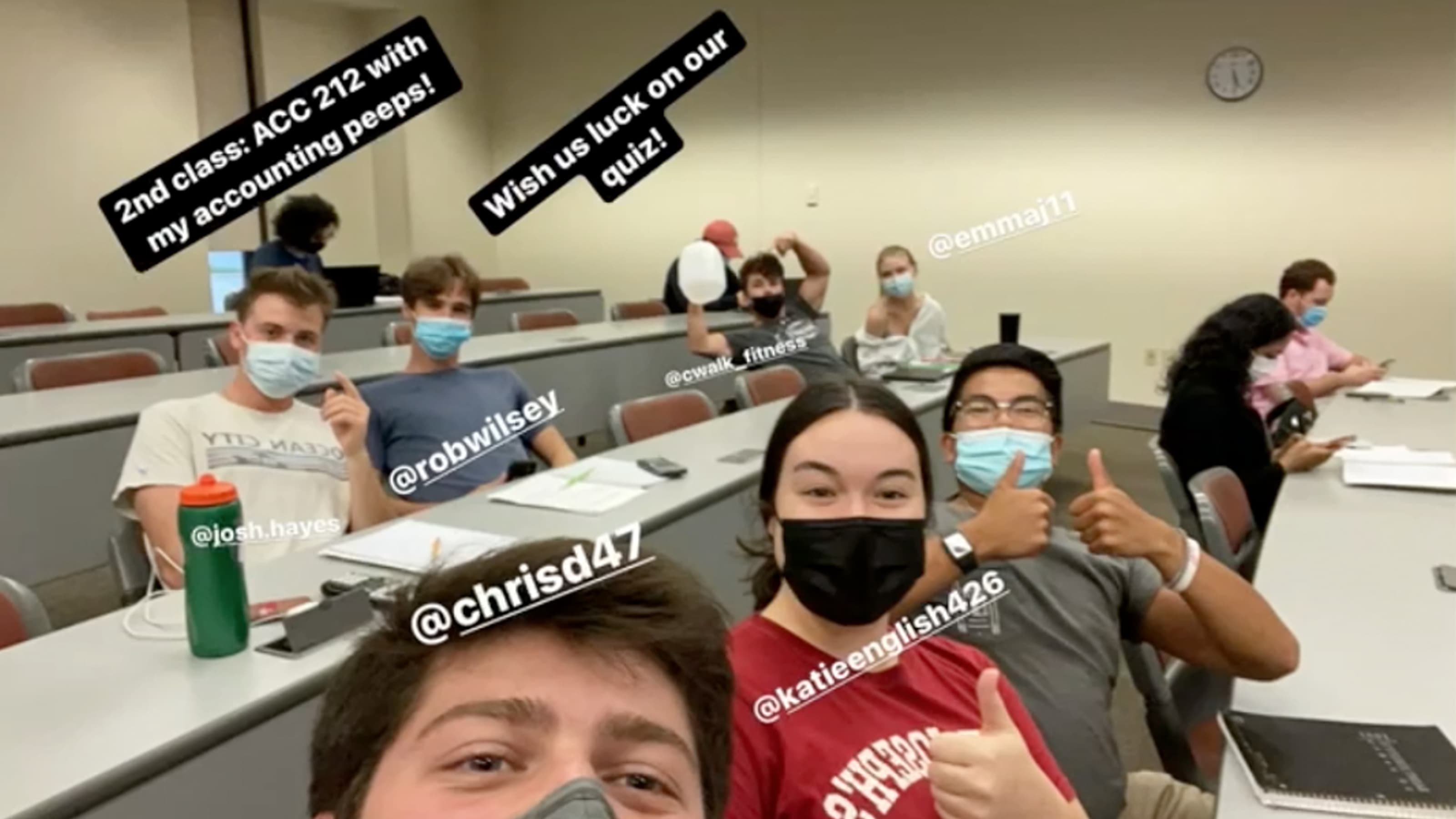 Students in masks give the camera a thumbs up in class