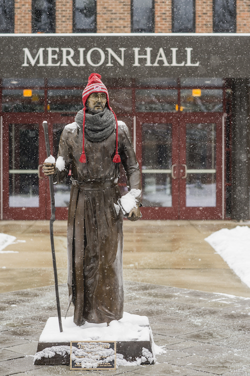 Saint Ignatius statue wears a winter hat while it snows
