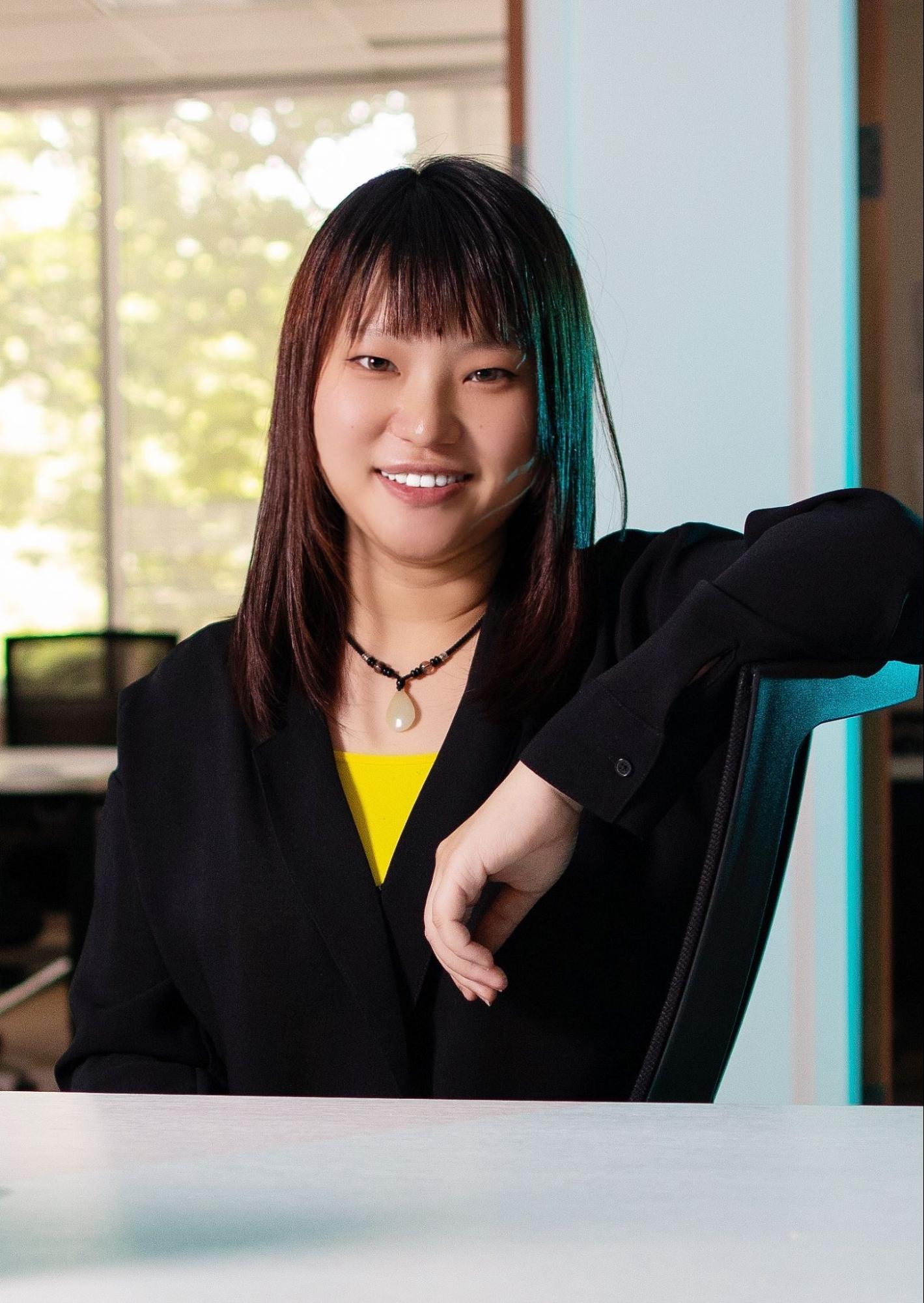 Liyuan Liu smiling at the camera with her arm leaning on the back of her chair