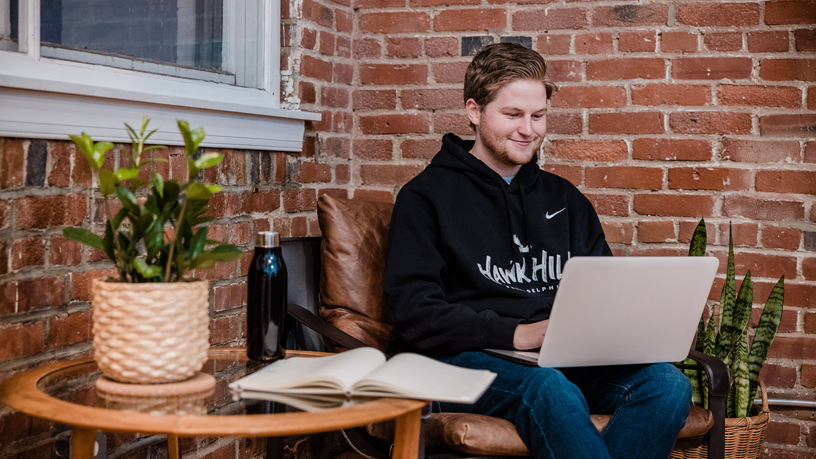 student wearing saint joseph's university hoodie, typing on a laptop