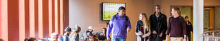 A group of four racially diverse students walk through a busy study area.