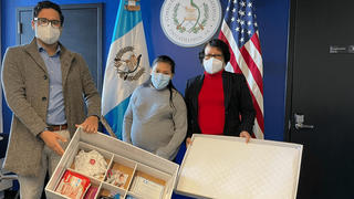 Two members of the Guatemalan Consulate present a pregnant woman with a baby box full of supplies.