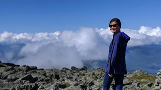 Dawn Cai standing on a mountain looking back at the camera