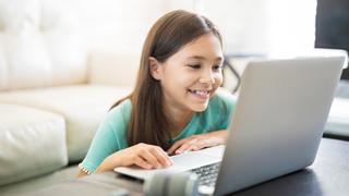 Child sitting at a table looking at a laptop and smiling.