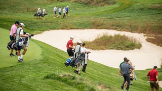 People with golf clubs and bags gather around golf hole.