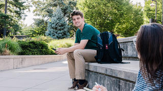 Young man sitting on stone bench outside, smiling.