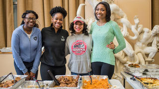 Four students standing behind trays of food.