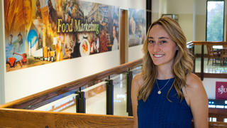 Claire Sylvester stands in front of a mural that reads "Food Marketing"