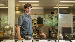 Petersen stands behind a table on which are placed several pieces of pottery.
