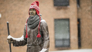 Statue of St. Ignatius covered in snow, with a red wool cap on.