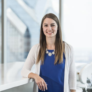 A student in a business casual outfit stands with a skyscraper behind her