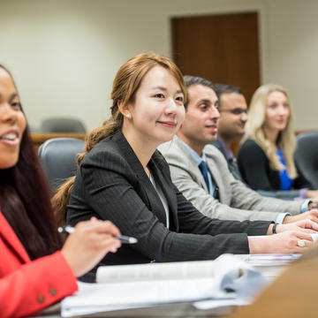 Students sit in a lecture class, one is smiling in the center