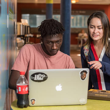A student helps another student as he works on a laptop