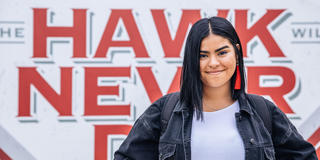 Saint Joseph's University student standing in front of a sign that reads: "The Hawk Will Never Die."