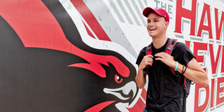 A young man walks in front of a mural on Hagan Arena featuring a painting of the Hawk.