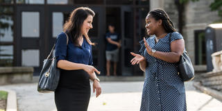 Two adult students smile at each other as they talk outside the student center on campus