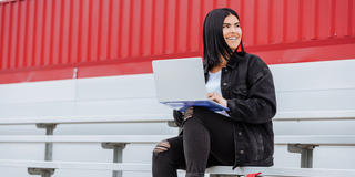 Saint Joseph's University Students smiling and sitting on the bleachers with her laptop.