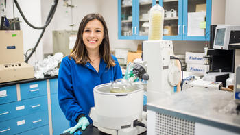 A woman in a blue shirt stands in a chemistry lab