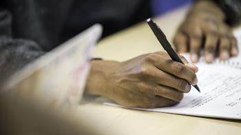 A person's hands are shown writing with a pen on a piece of paper