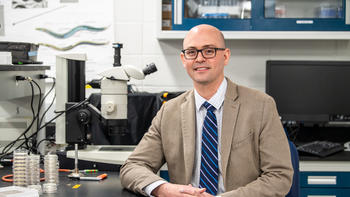 Matthew Nelson Ph.D. sits in the lab wearing a tan blazer and blue tie
