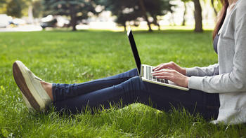student sitting in the grass with laptop