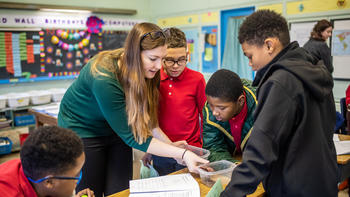 A young woman shows an experiment to three elementary aged boys