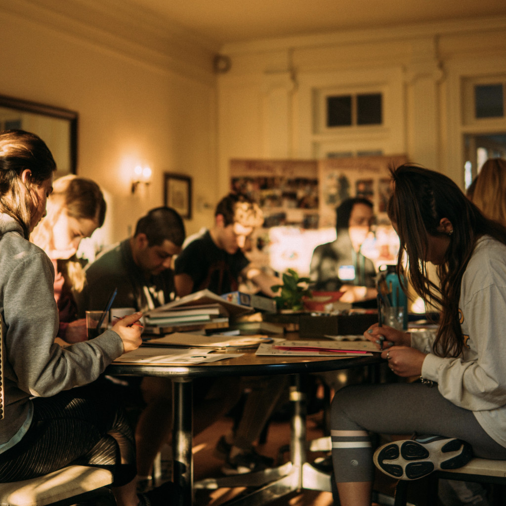 A group of students sitting around a table with bowed heads