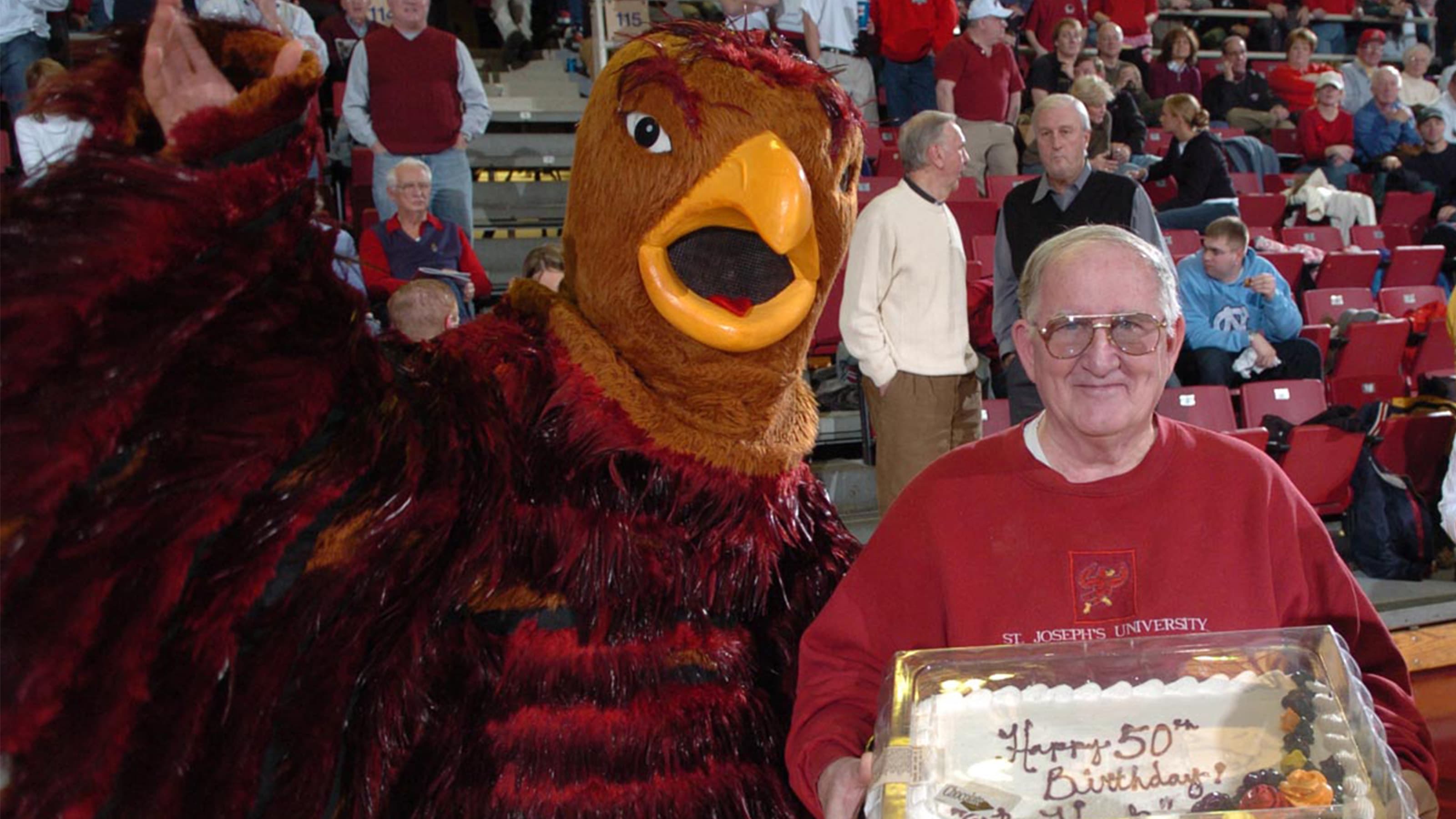 The Hawk mascot standing next to alumnus Jim Brennan holding a birthday cake