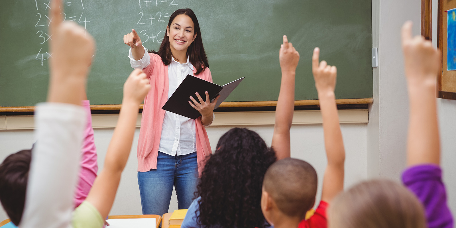 teacher in front of a room full of students with hands raised