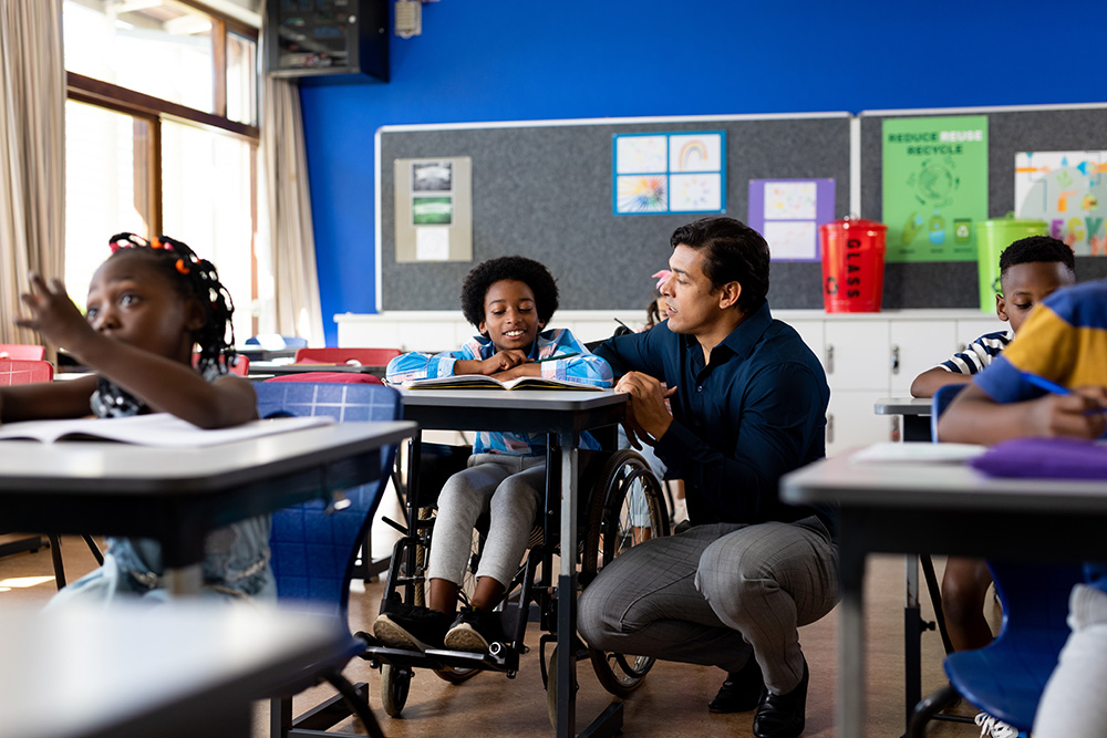 teacher bending down at the desk of a student in a wheelchair