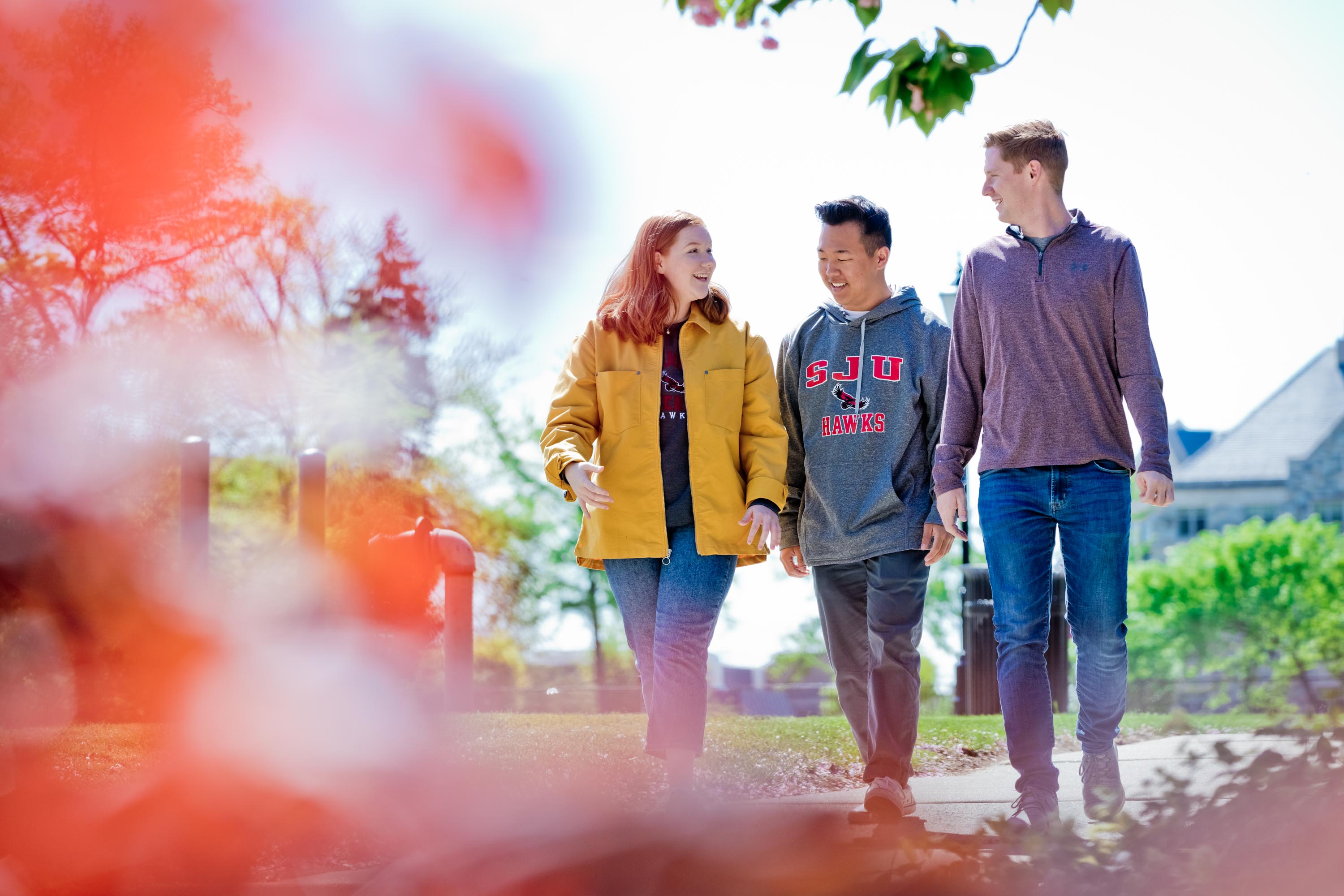 three students walk across a flowering campus