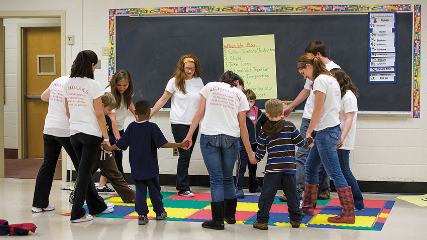 adults holding hands with children in a classroom