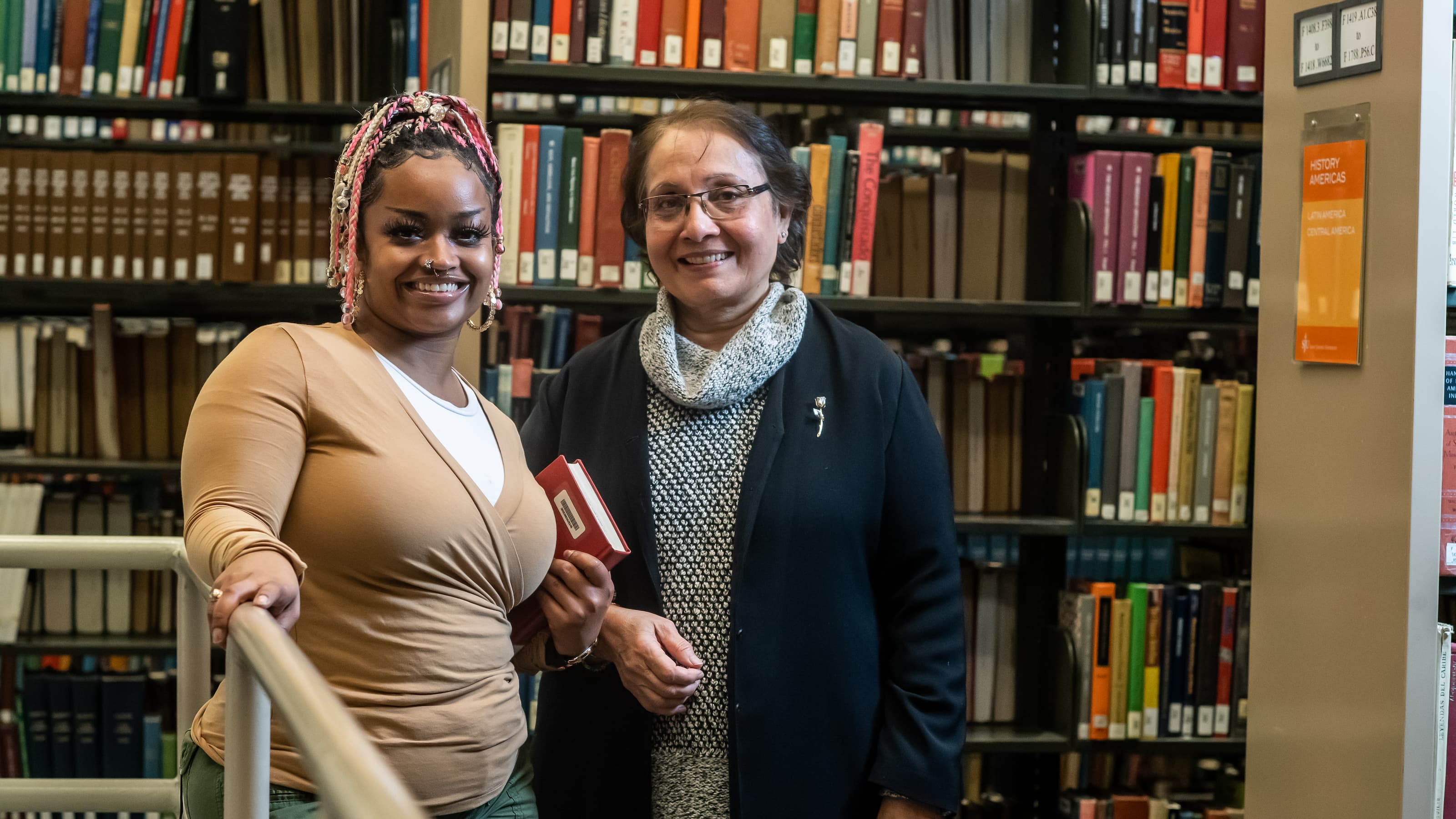 A student and professor are smiling in the library