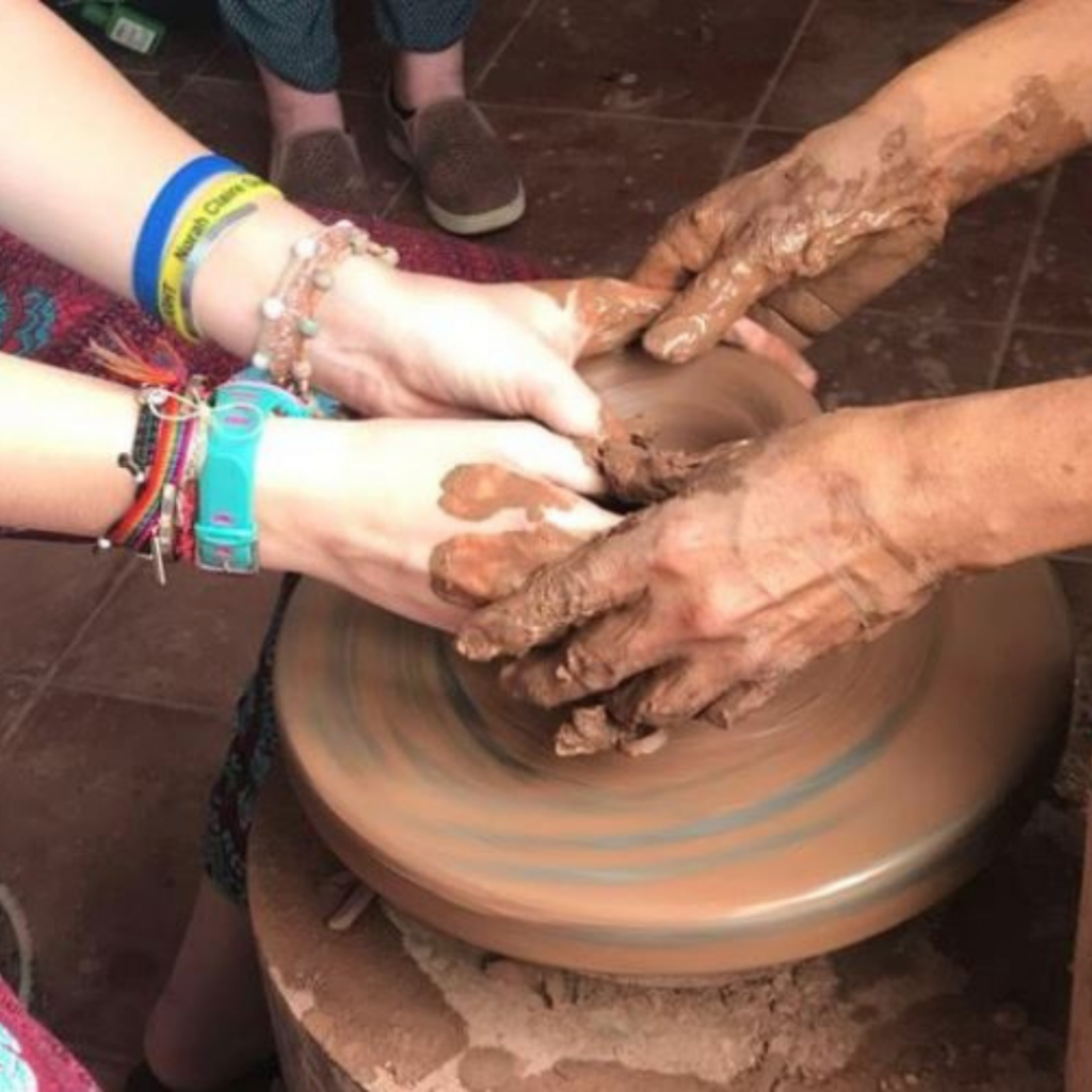 Clay being moulded on a pottery wheel by two individuals