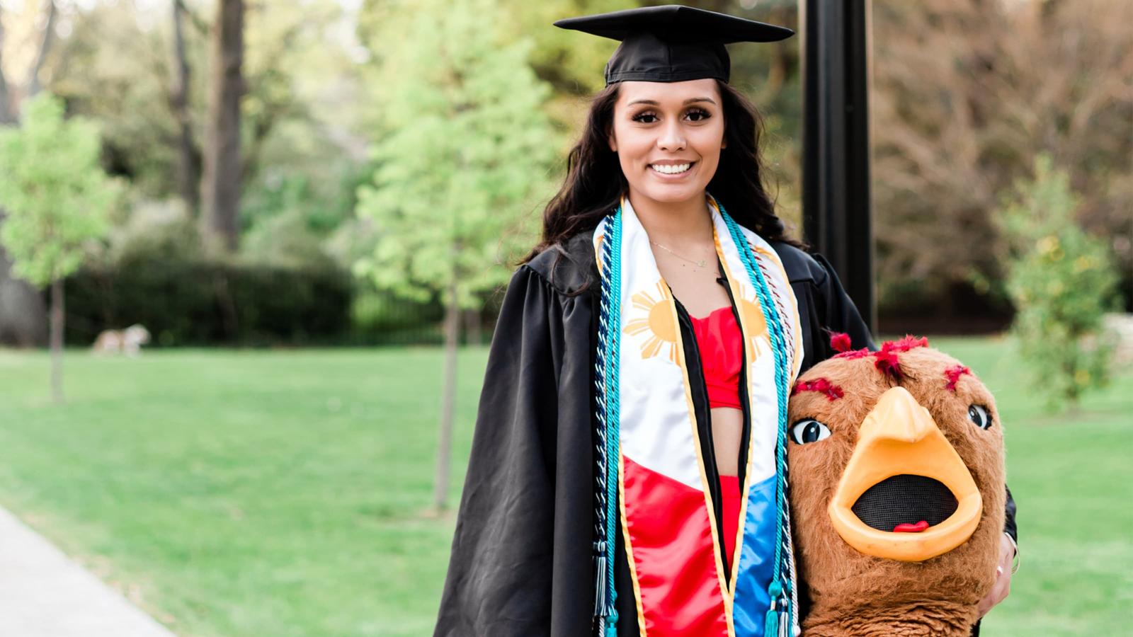 Asia Whittenberger holding the Hawk mascot head in her cap and gown