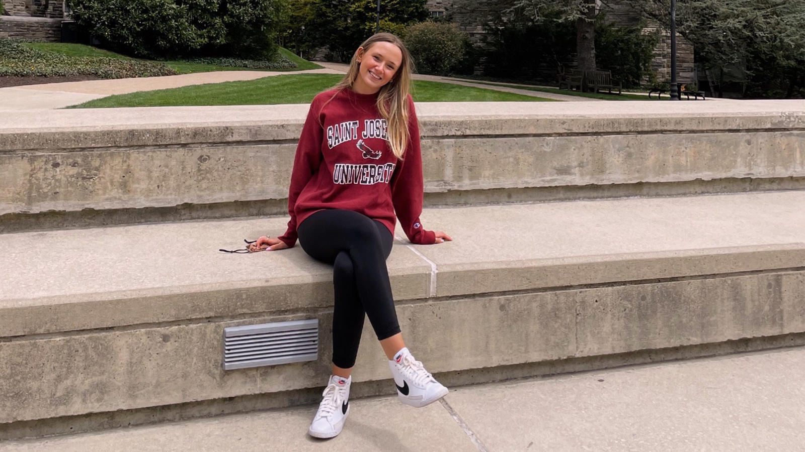 Female student sitting on campus in Saint Joseph's sweatshirt