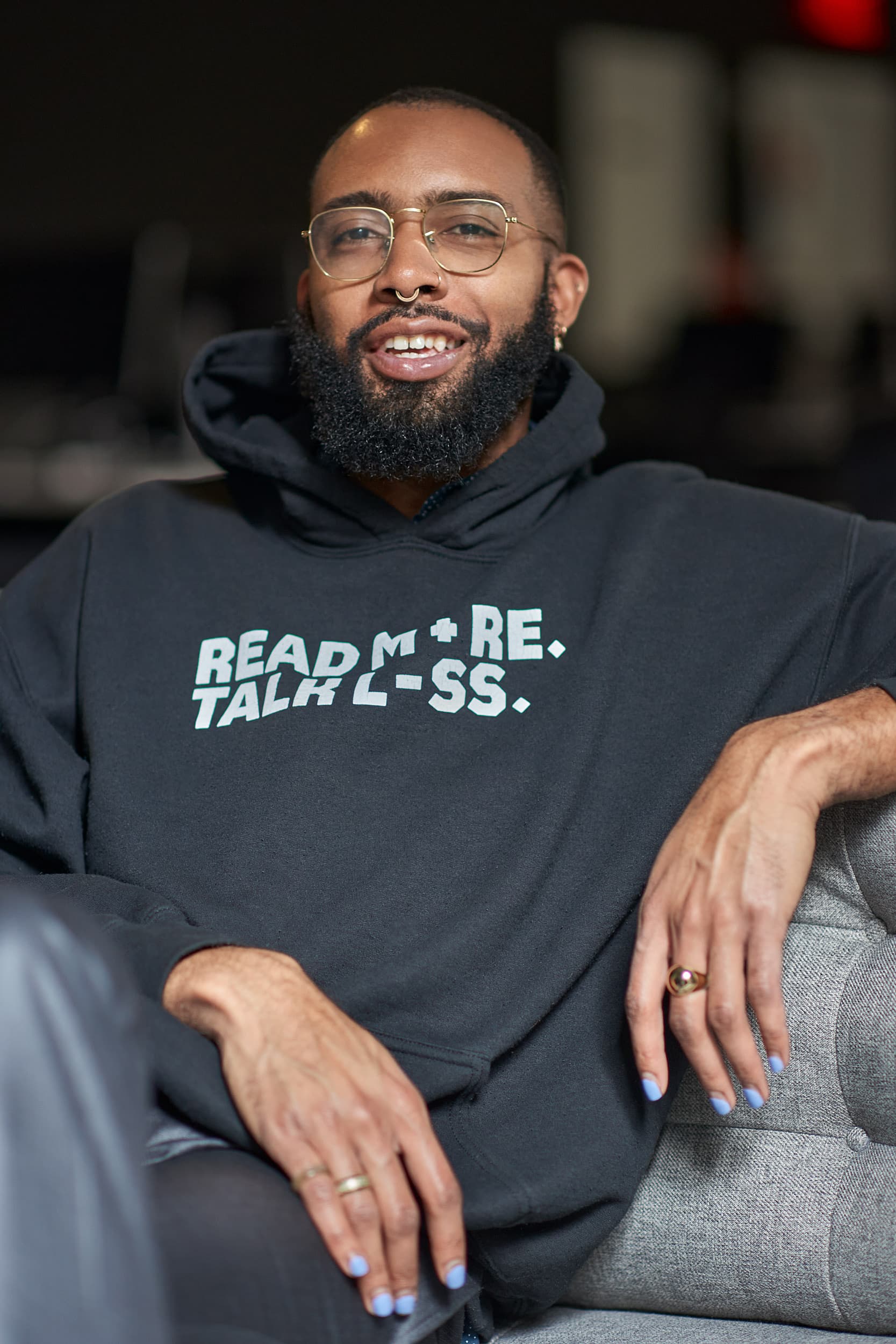 Alumnus Joseph Thomas seated in a black sweatshirt that says "Re+d More, Talk L-ss"