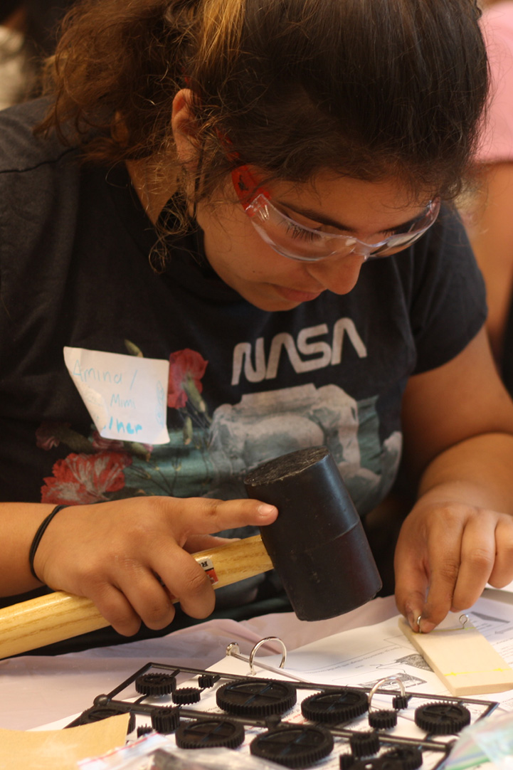 Student in googles working on a physics experiment with a rubber mallet