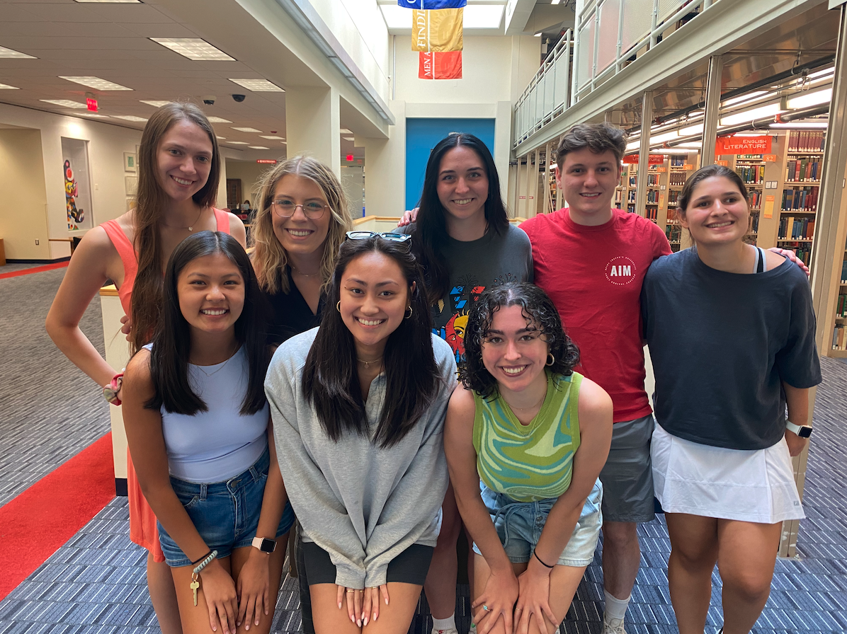 A group of students standing together in front of library book stacks