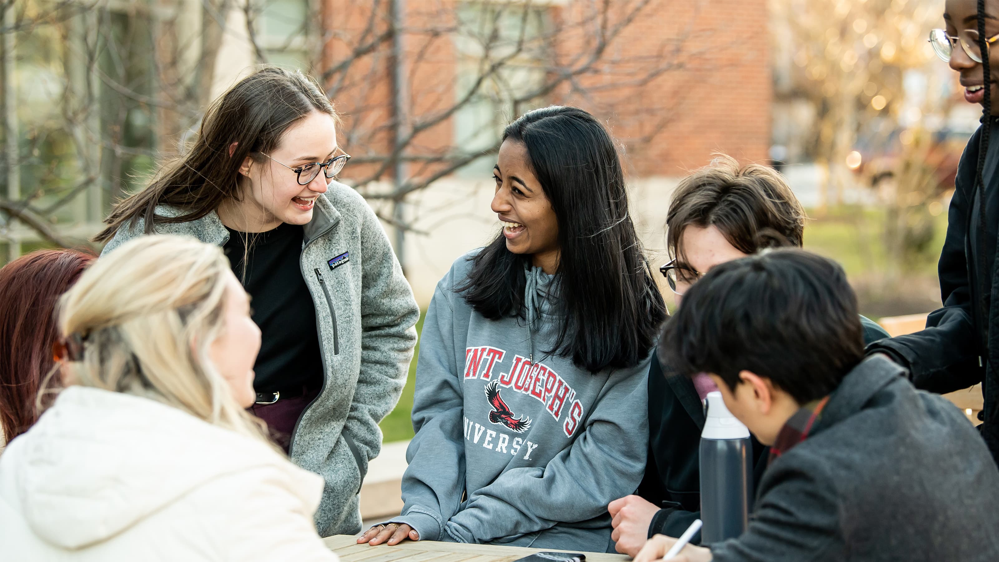 A group of students talking and laughing outside at a picnic table