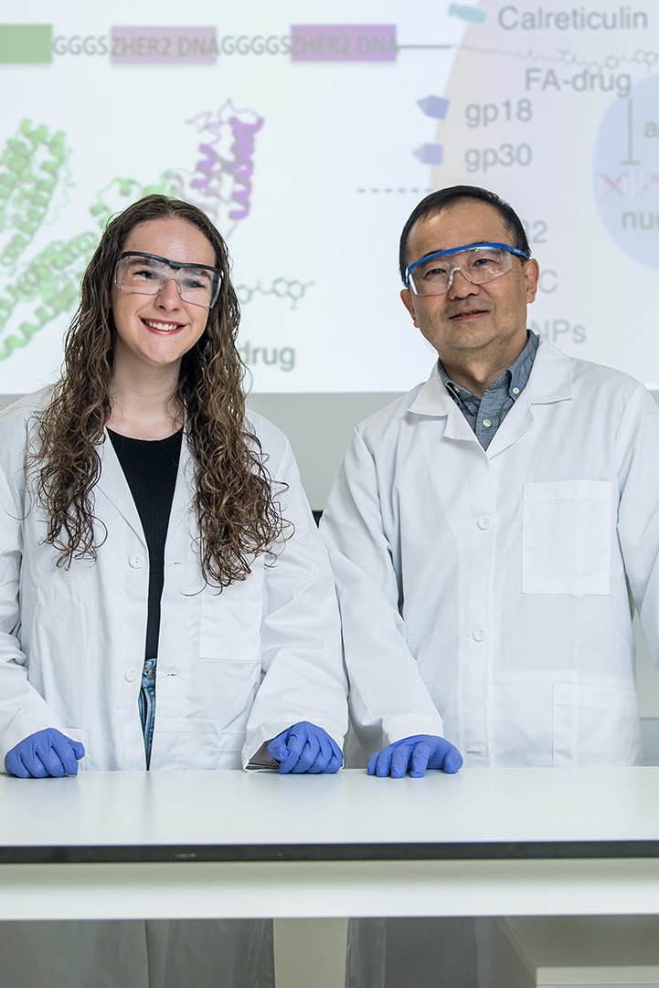 Zhiyu Li and Hailey Swaldi pose in the lab wearing lab coats and goggles