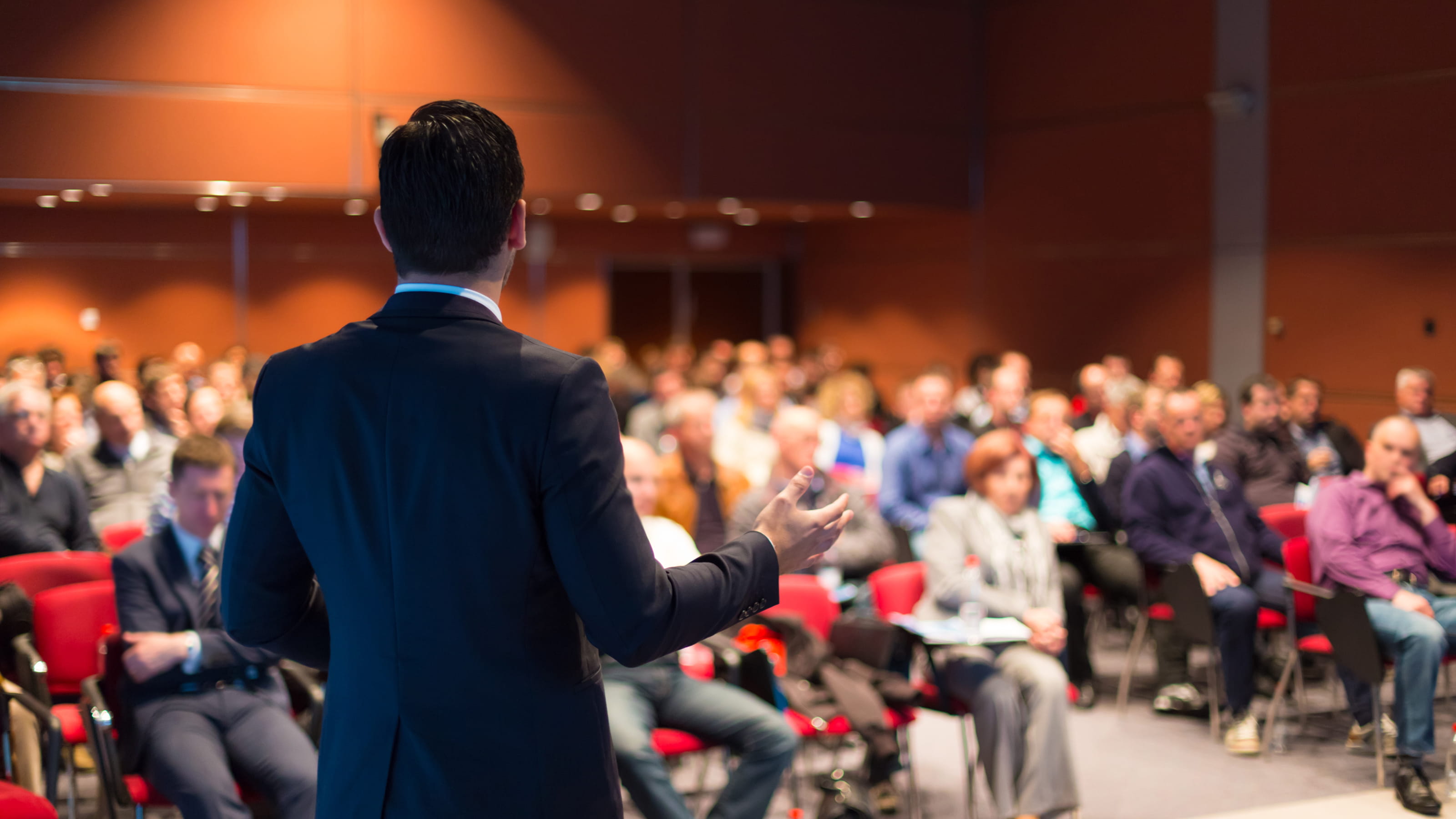 Person lecturing in a hall in front of people in chairs